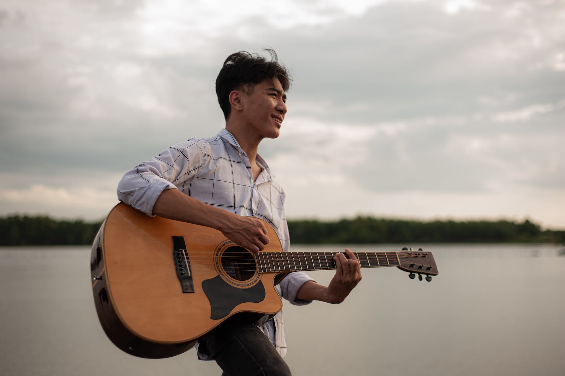 young man playing on acoustic guitar by the lake